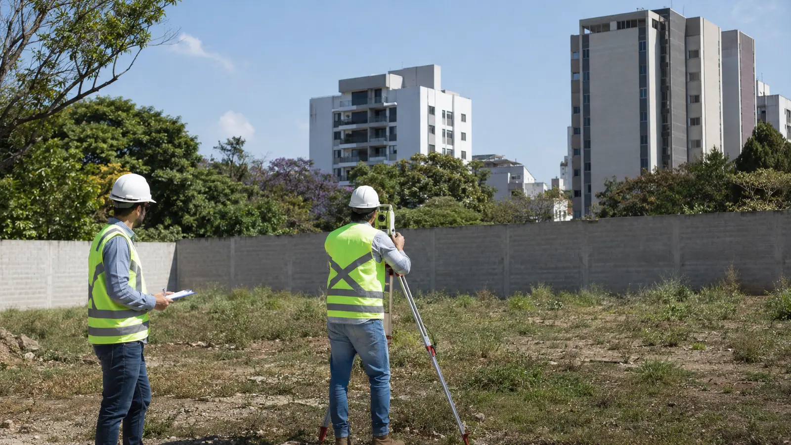 Engenheiros avaliando um terreno urbano com prancheta e equipamento topográfico